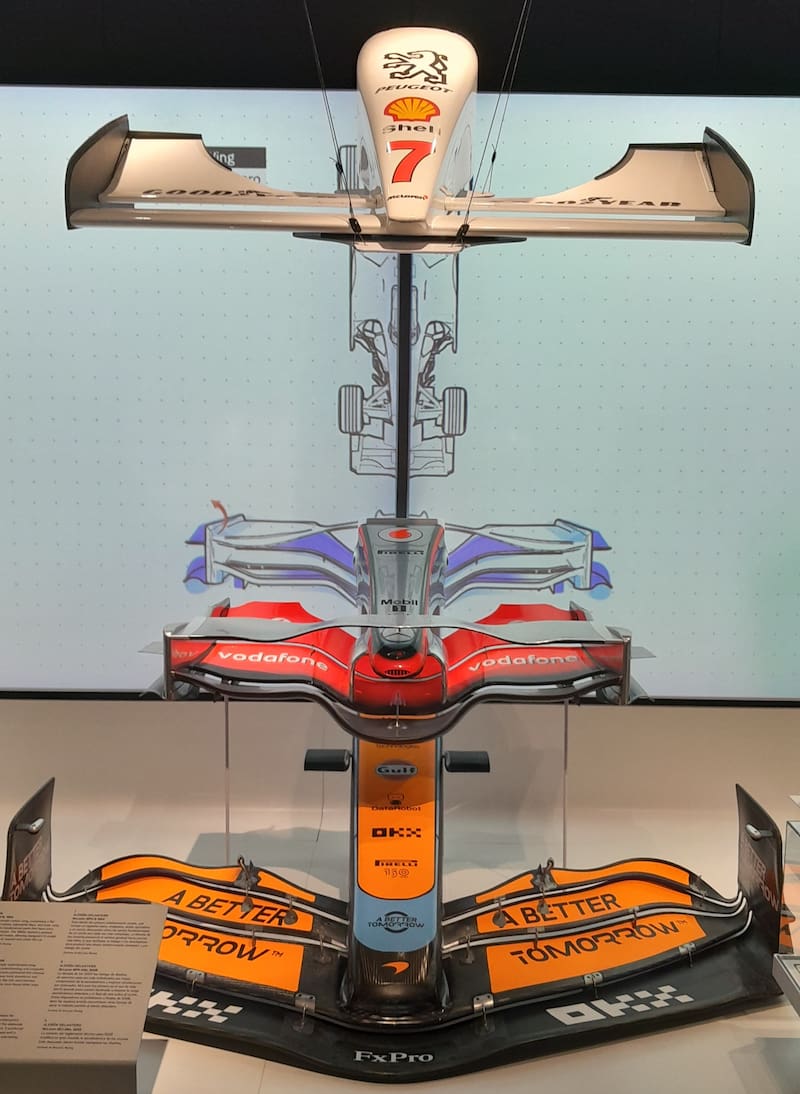 Three F1 front wings on display from different eras of the sport, with one from the McLaren MP4/9, one from the MP4-23A, and one from the MCL36A.