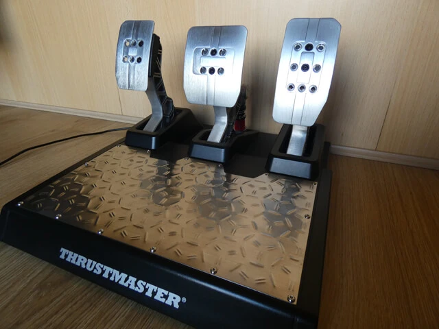 Thrustmaster T-LCM pedals on a wooden floor with a wooden background.