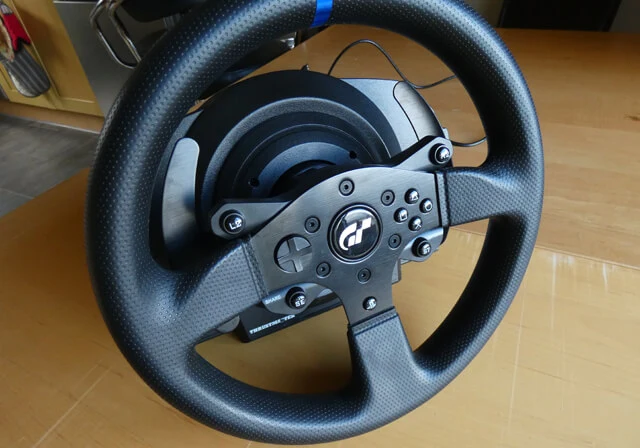 Thrustmaster T300RS GT edition sim racing wheel on a wooden table, showing the wheel rim and the wheel base.