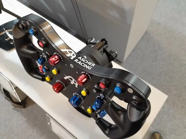 Ascher Racing sim racing wheel rim on a display stand showing off all the various buttons, dials and switches.