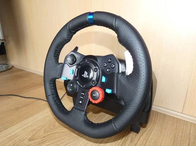 Logitech G29 sim racing wheel for PlayStation sitting on a wooden floor with a wooden background.