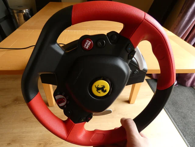 Thrustmaster Ferrari 458 Spider sim racing wheel on a wooden table with a hand showing the limited range of rotation of the wheel.