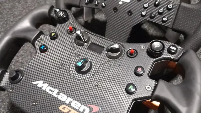 Close up of the Fanatec McLaren GT3 sim racing wheel showing the buttons and rotary encoders with a Fanatec CSL P1 V2 wheel in the background.