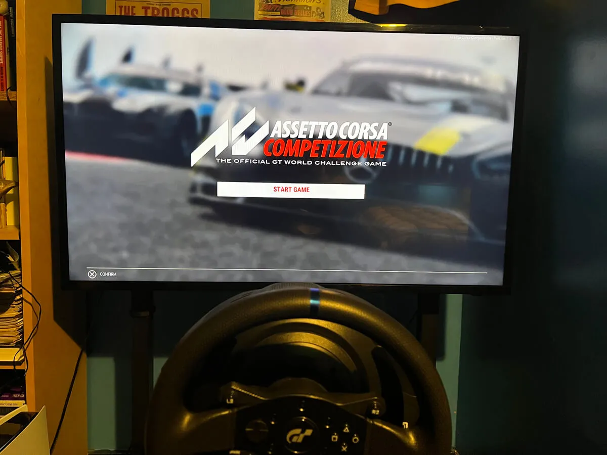 Next Level Racing sim racing monitor stand holding a 42 inch TV with Assetto Corsa Competizione on the screen and a Thrustmaster T300 RS wheel in the foreground.