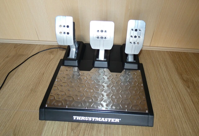 The Thrustmaster T-LCM sim racing pedals with a wooden background.